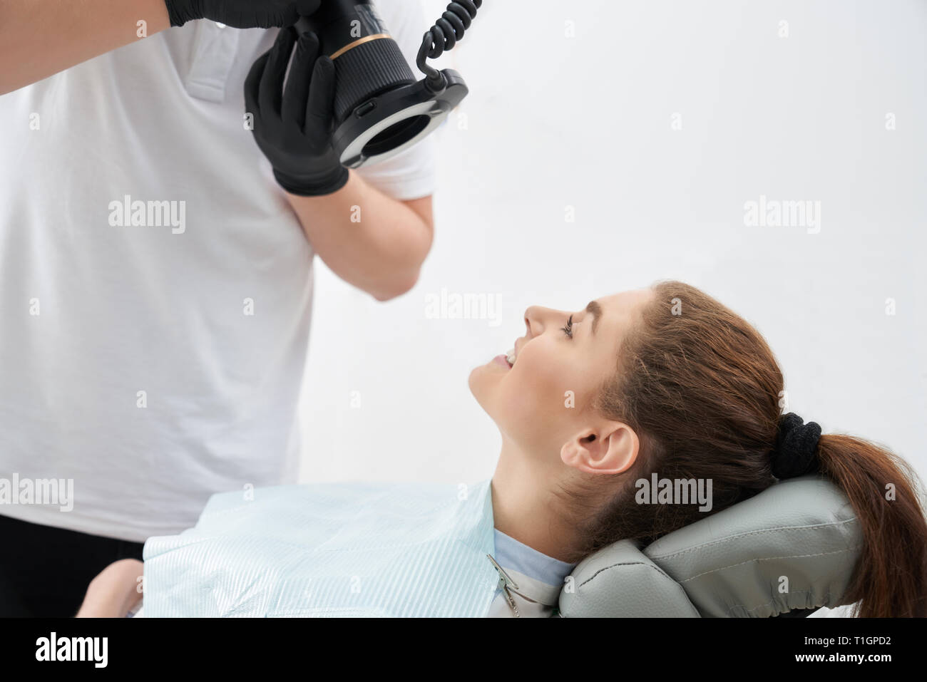 Seitenansicht der jungen Patientin sitzen in Zahnarztpraxis und schönes Lächeln nach dem Verfahren. Arzt unter Foto von Ergebnis nach dem Bleichen der Zähne. Konzept der Zahnheilkunde. Stockfoto