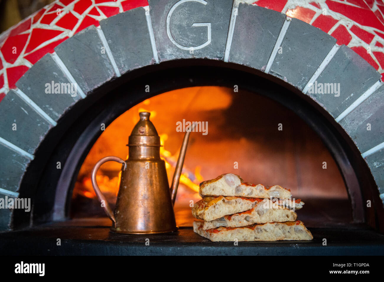Scheiben der traditionellen römischen Stil Pizza im Mund der Holzofen in einer Trattoria, Pizzeria mit Messing Olivenöl Flasche Backofen Stockfoto