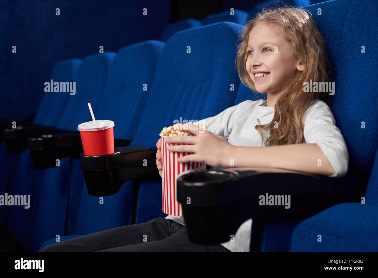 Fröhlicher, lustiger Mädchen, dass Schaufel mit Popcorn, Film oder ein Cartoon in Kino. Schöne blonde Mädchen lächelnd, genießen Film. Stockfoto