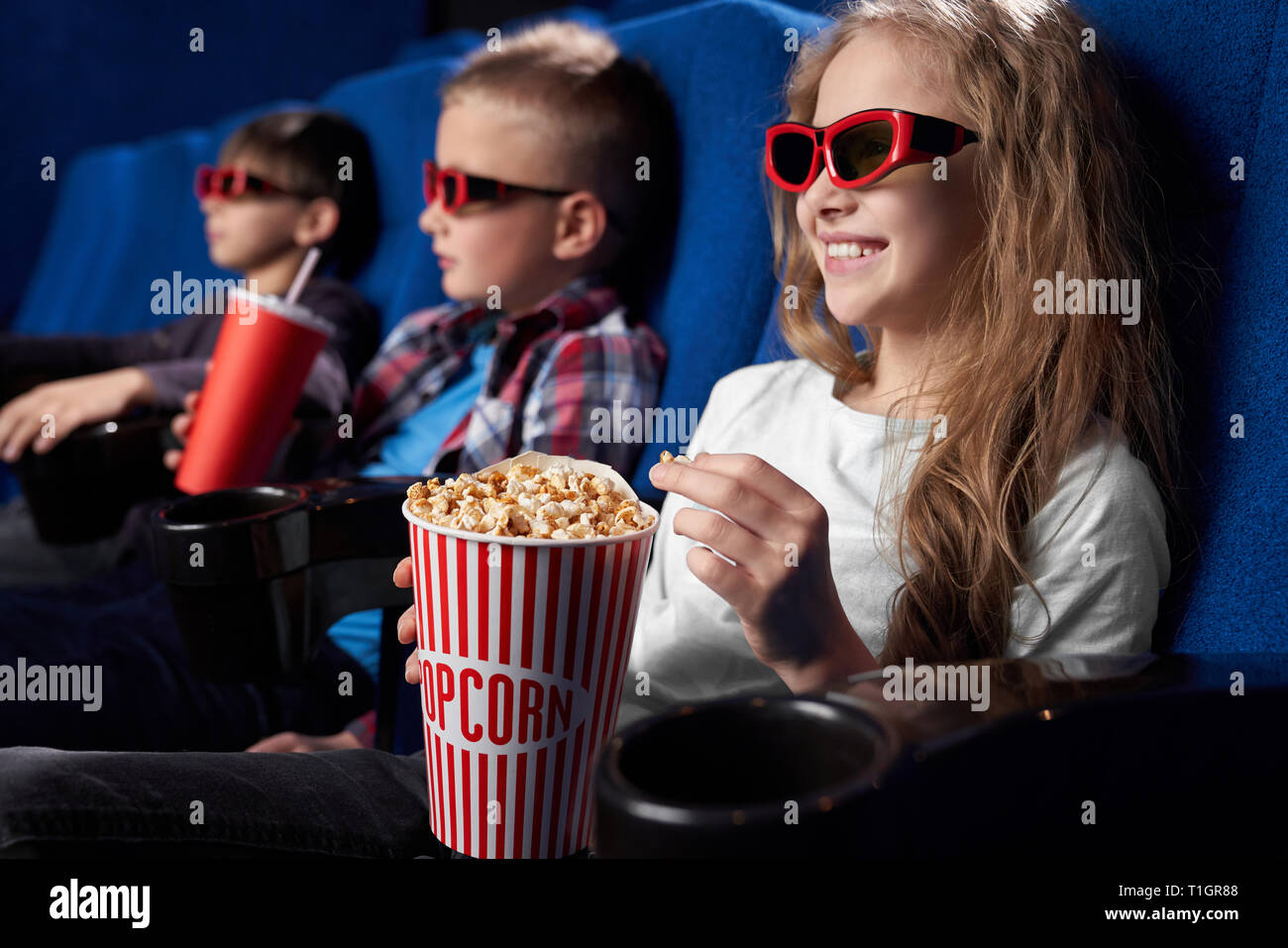 Schöne, hübsche Mädchen sitzen mit Freunden in ciname Theater, Film oder Cartoon. Fröhliches Mädchen lächelnd, holding Popcornwanne, aufzupassen Film. Stockfoto