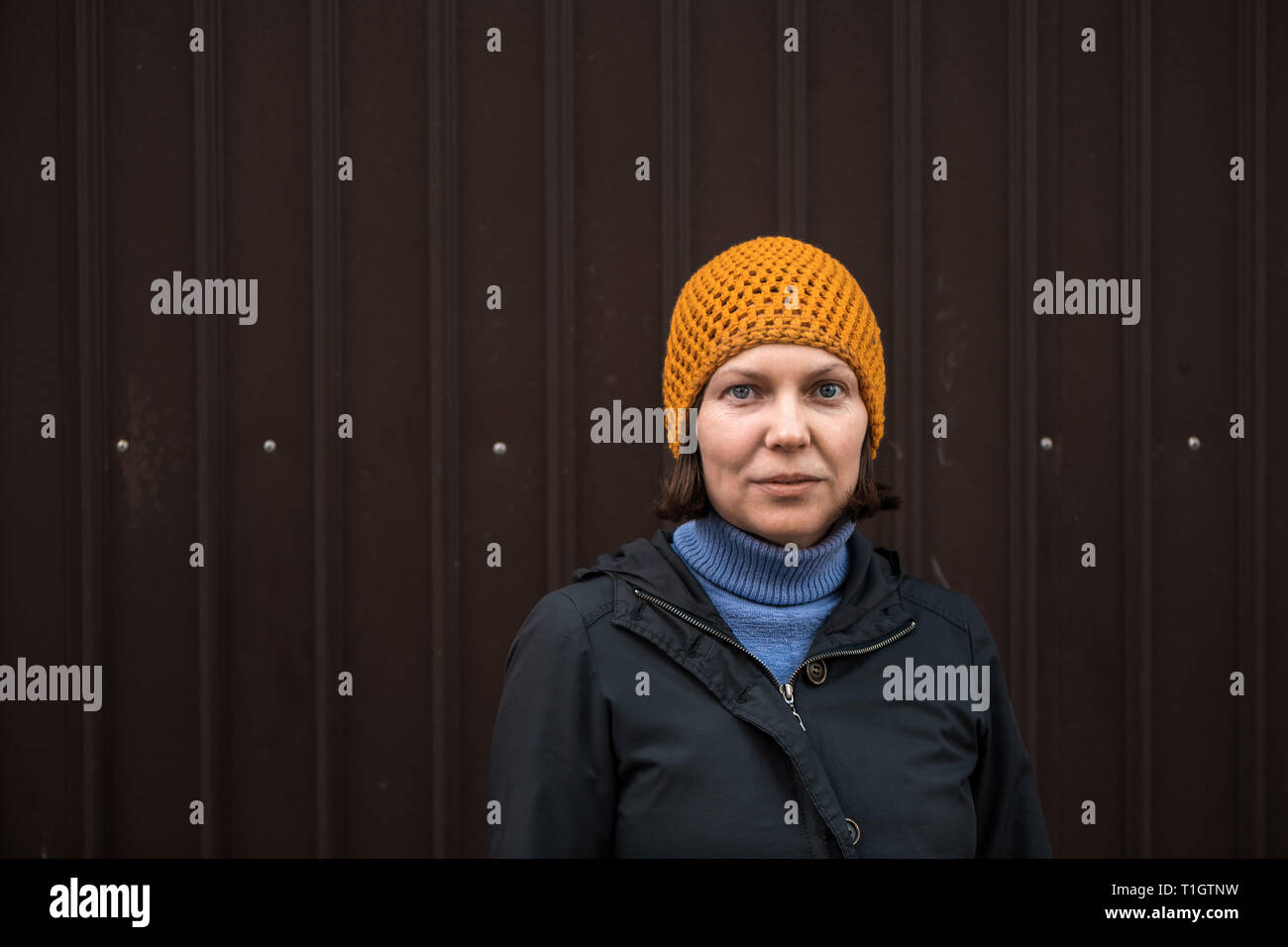 Schöne Frau in 40s, urban Porträt retro getönt. Weibliche Person tragen gelbe Kappe und warmen Herbst Jacke posing und Kamera. Stockfoto