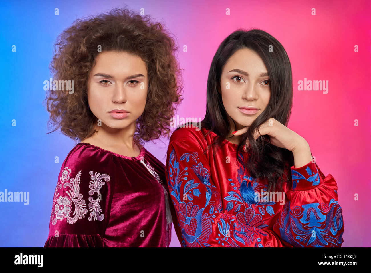 Modelle tragen in den traditionellen roten Kleidern posieren. Bezauberndes Mädchen mit lockigem Haar und elegante brunette auf Kamera schaut. Frauen tragen in bestickte Kleidung, Atlas Gewebe. Stockfoto