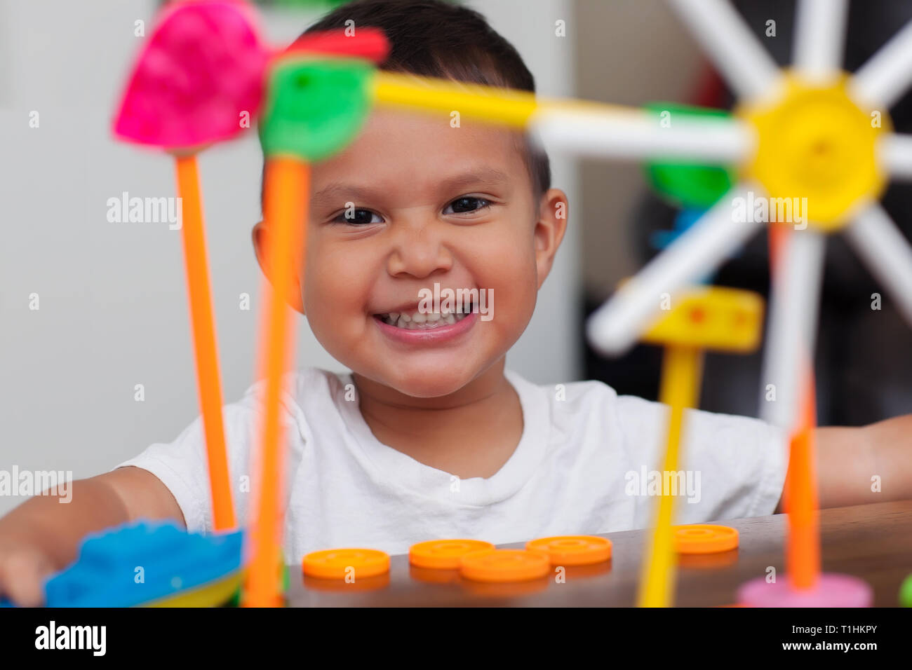 Ein Hispanic junge mit großen Lächeln, während er mit bunten Gebäude Spielzeug spielt und lernt, sich mit elementaren manipulative Spielzeug zu zählen. Stockfoto