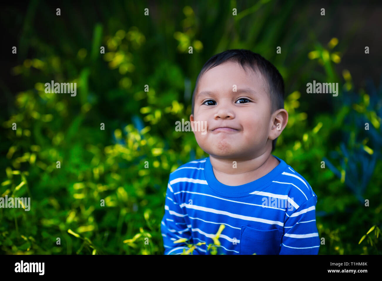 Einen gesunden Jungen suchen, um sich in der Bewunderung mit einer positiven Einstellung und zufriedenen Lächeln sitzt in einem Feld von gelben Blumen beim Tragen eines gestreiften Stockfoto