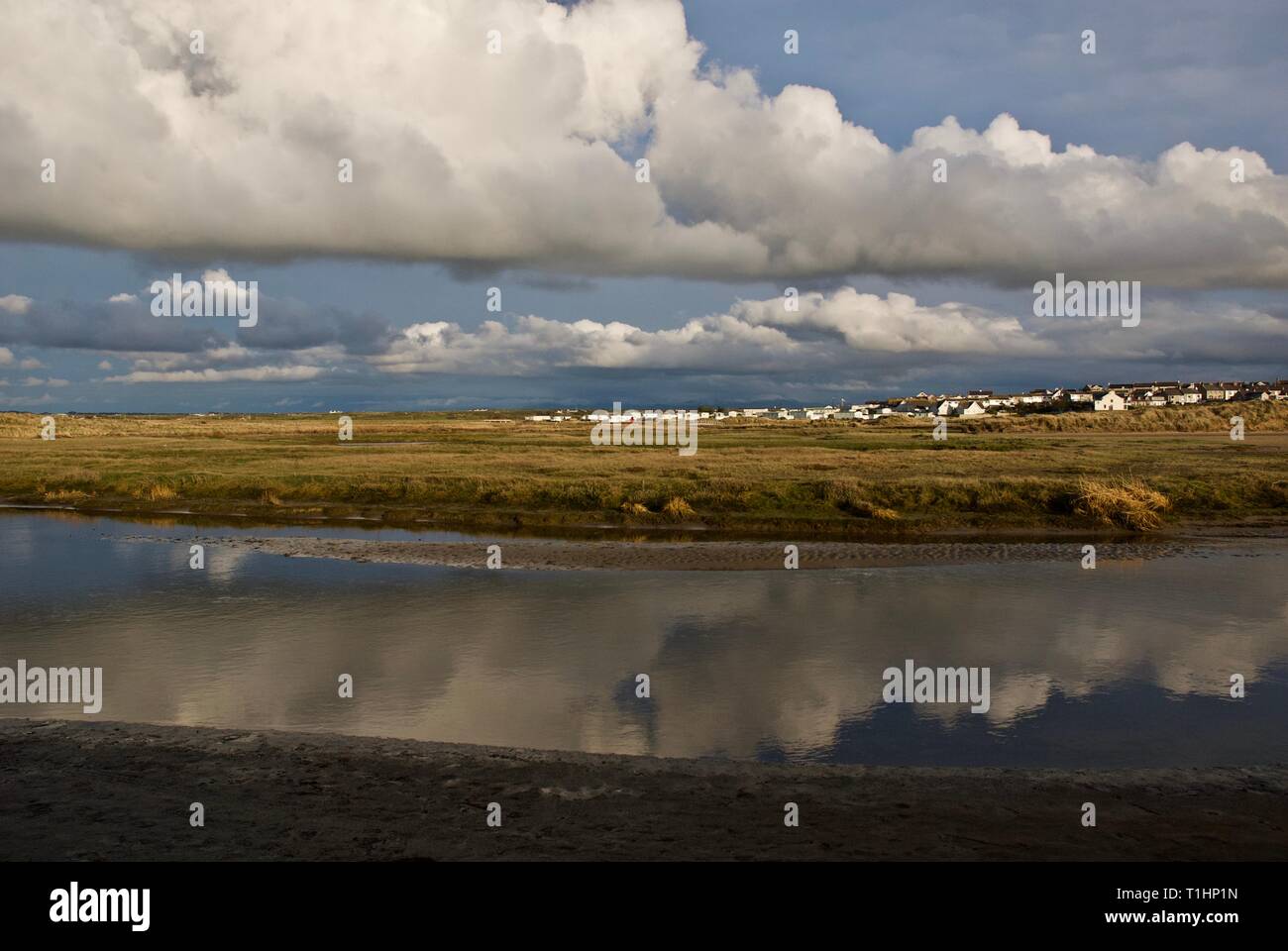 Blauer Himmel und Wolken in den stillen Wassern des Afon Crigyll wider, mit der das Dorf in der Ferne, Rhosneigr, Anglesey, North Wales, UK Stockfoto