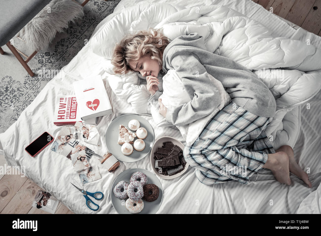 Frau im Bett liegend in der Nähe der Bücher und Essen nach Auseinanderbrechen Stockfoto