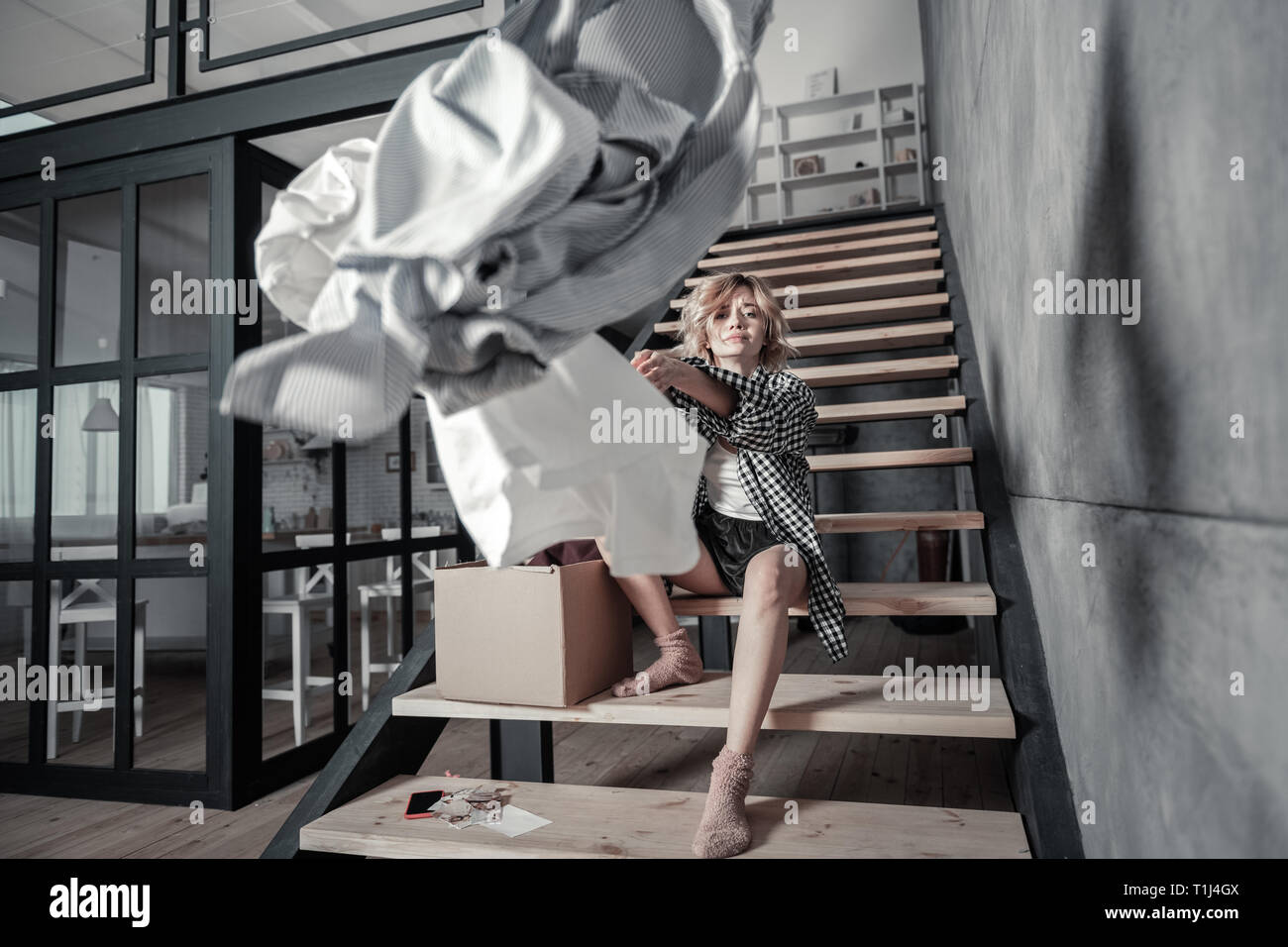 Einsame Frau auf der Treppe, zu Hause zu sitzen und Kleidung zu werfen Stockfoto