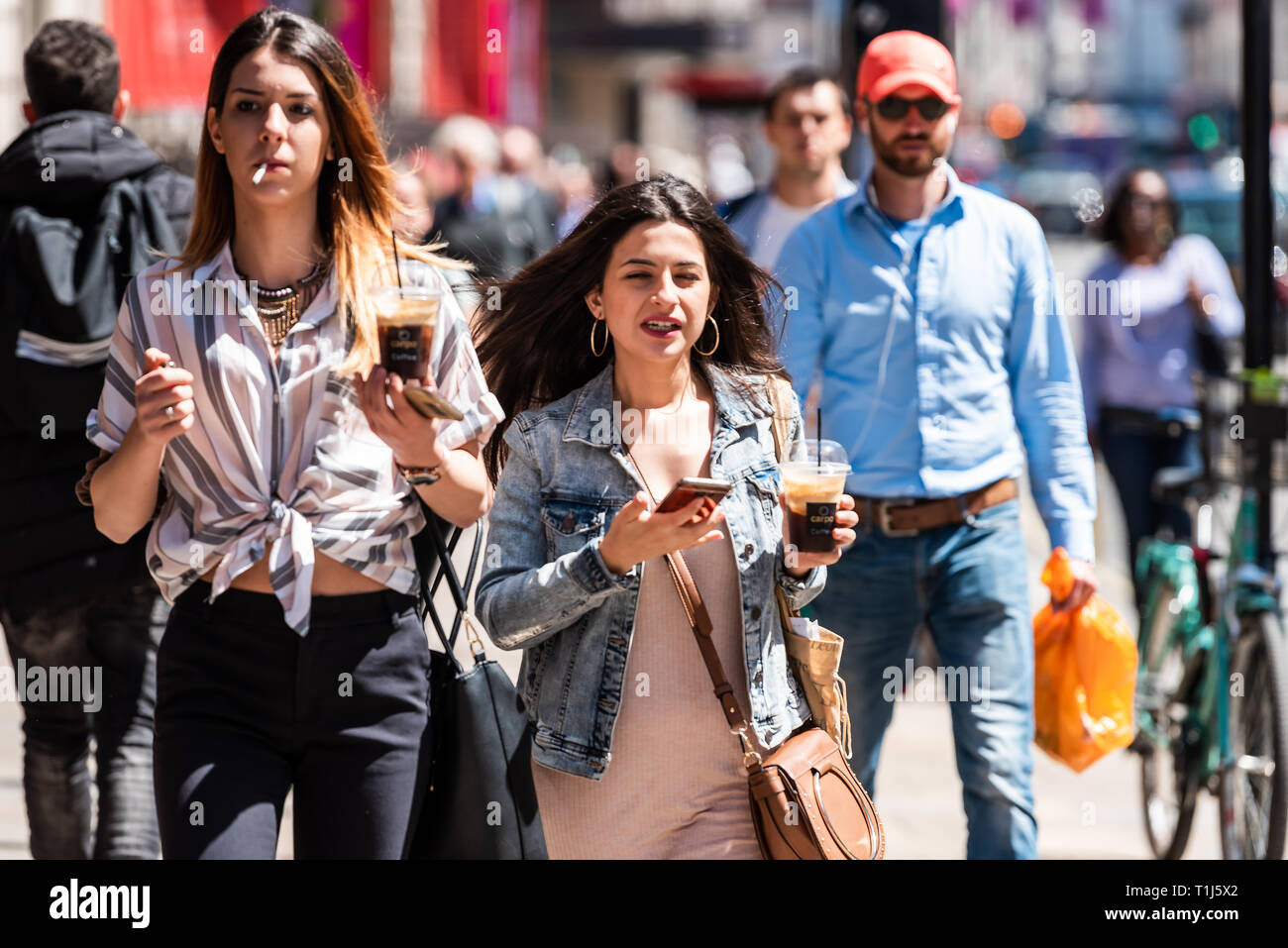 London, Großbritannien, 22. Juni 2018: Leute, Touristen oder lokalen stilvolle junge Frauen gehen mit Telefon und Eiskaffee auf Gehweg Pflaster auf der Piccadilly Regent Stockfoto