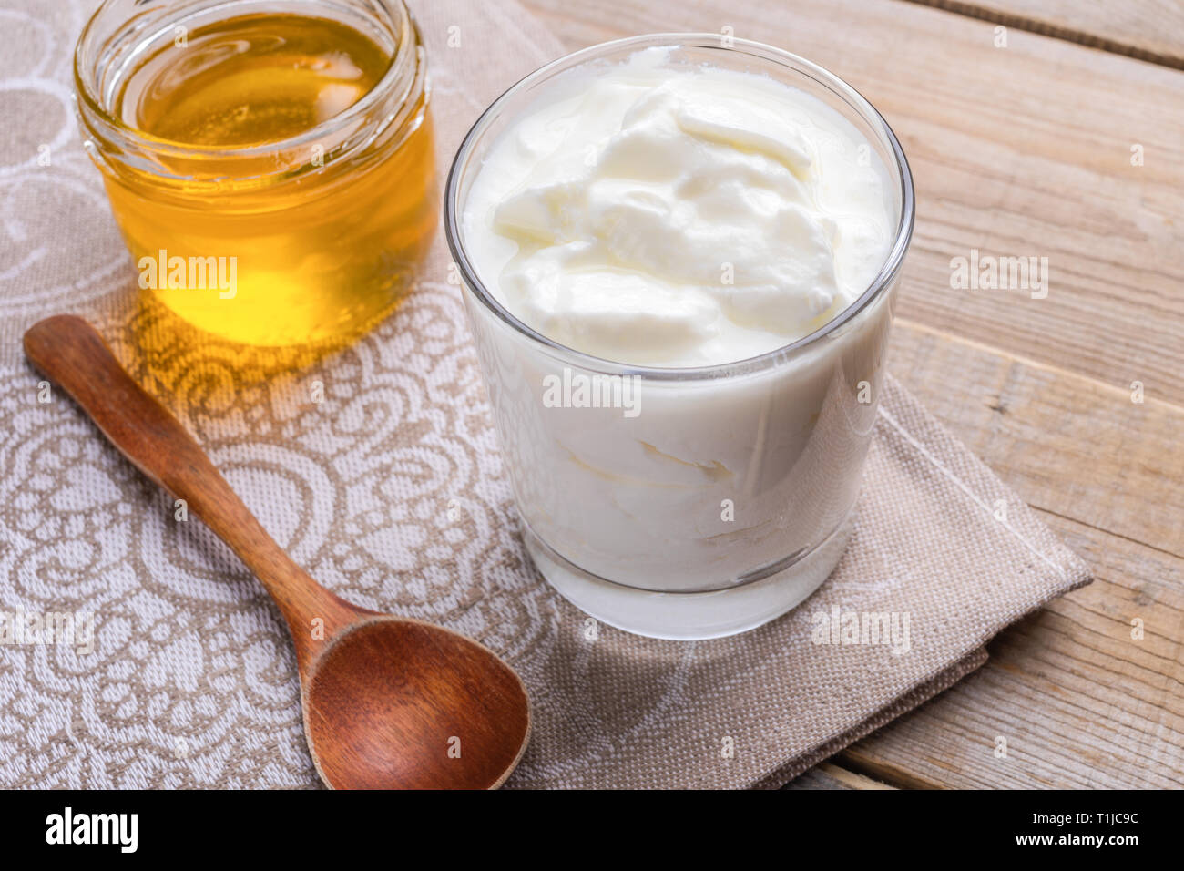 Transparente Glas fat hausgemachte Joghurt mit Löffel und Krug Honig steht auf Holztisch. Stockfoto