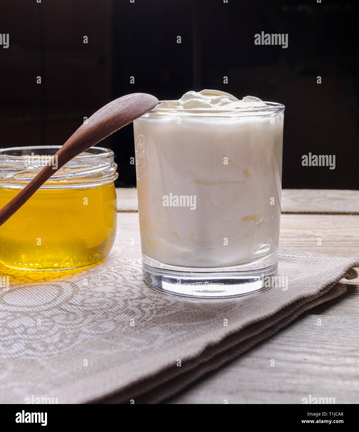 Glas Joghurt mit Löffel aus Holz und Glas Honig auf Holztisch auf dunklem Hintergrund. Stockfoto