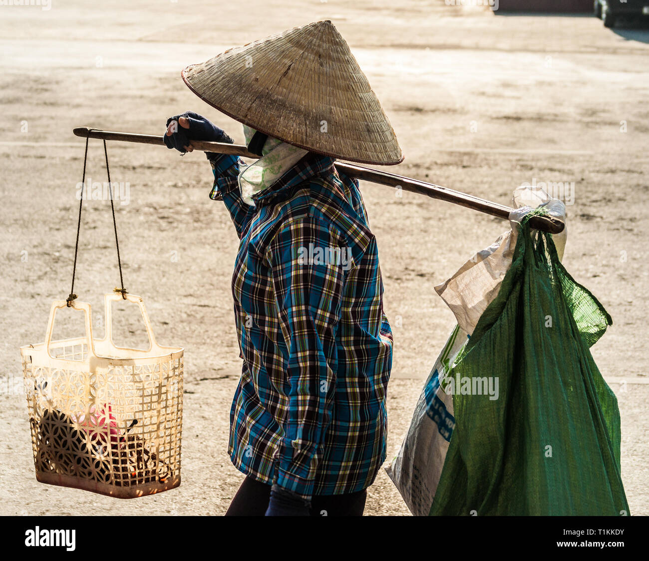 Stock Bild unkenntlich Vietnamesische mit konischen Hut trägt ein Joch auf der Schulter entlang der Straße. Profil Blick eines Menschen mit konischen Hut in Stockfoto