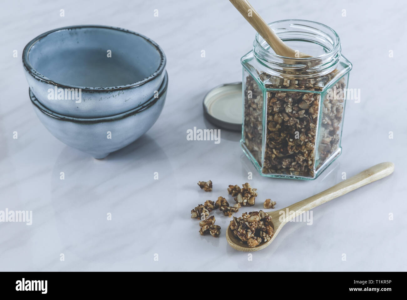 Hausgemachten gesunden und nahrhaften Frühstück Müsli in einem Glas mit Holz, Löffel und blau Keramik Schalen auf marmorboden Küchentisch im Morgenlicht Stockfoto