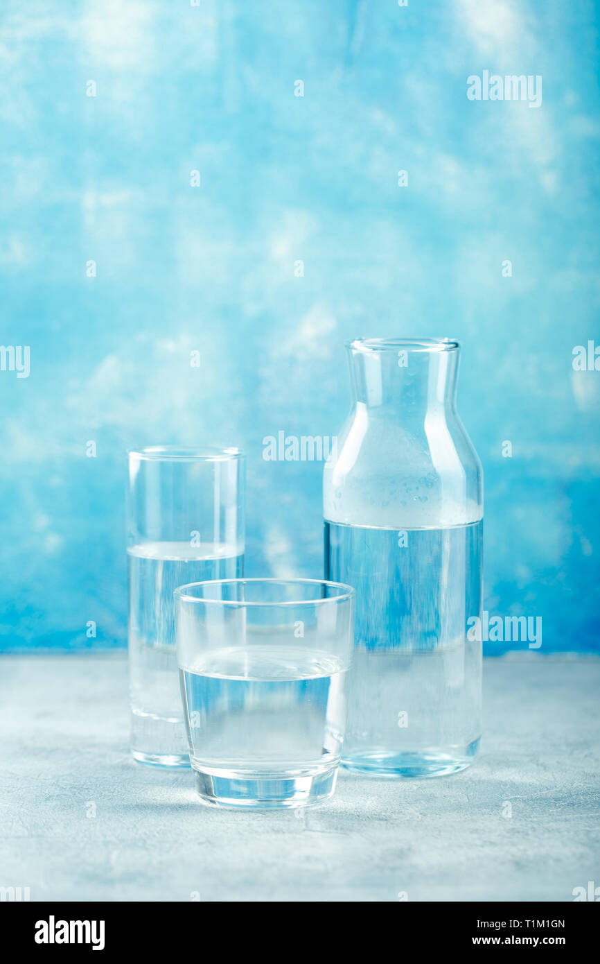 Gruppe von leeren Gläsern und Flaschen mit klarem Wasser auf blauem Hintergrund Stockfoto