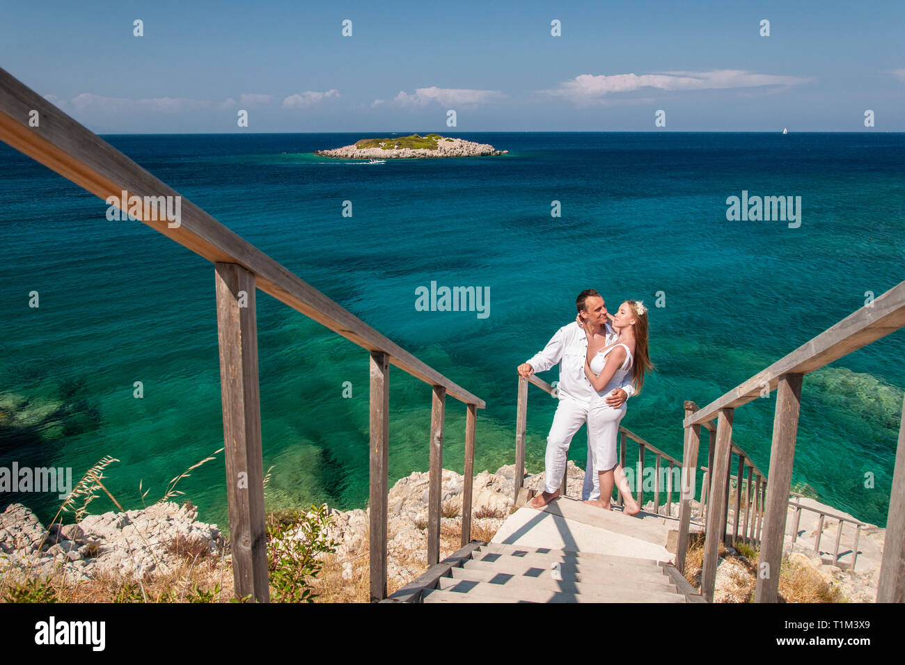 Romantische Ansicht der glücklichen Paare in weißen Kleidern kuscheln und stehen auf felsigen Küste. Malerische Seenlandschaft von blauem Meer und die kleine Insel. Konzept der Ho Stockfoto