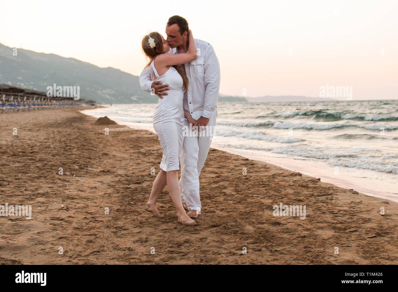 Romantische Ansicht der Paare in der Liebe, sie küssen, halten in den Armen und Spaziergang durch Sandstrand. Schöne Landschaft von Meer bei Sonnenuntergang. Konzept der Hone Stockfoto