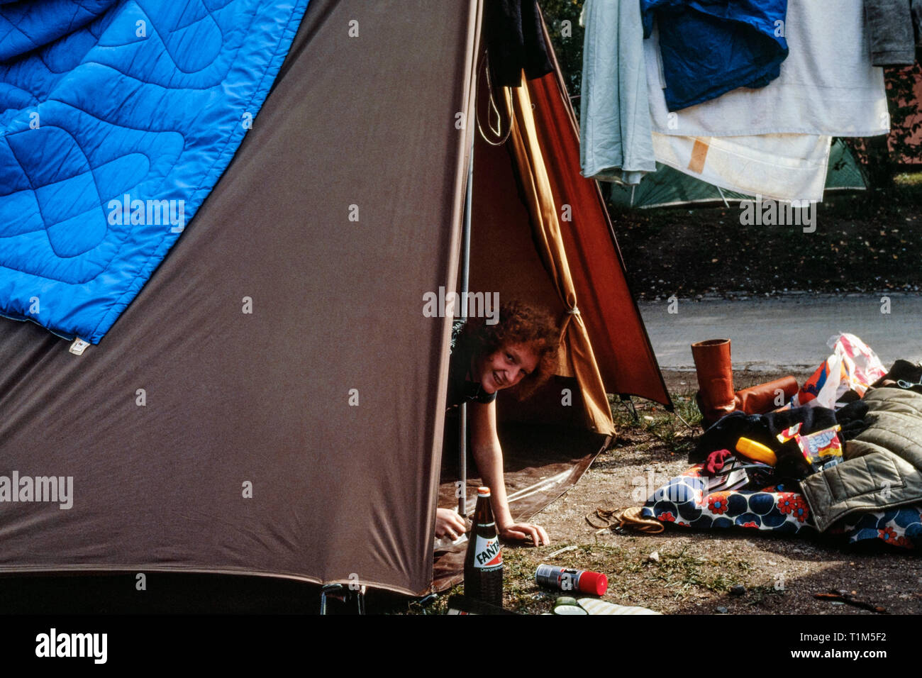 Lächelnde junge Frau aus Zelt Eingang und wischen Sie das Wasser vom schweren Regenguß 1980 München Deutschland suchen Stockfoto