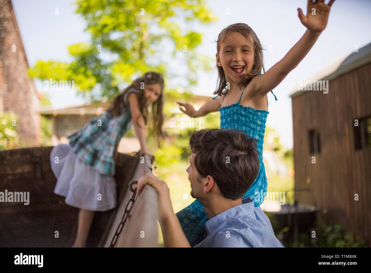 Portrait verspieltes Mädchen mit Vater und Schwester auf Wagen im Hof Stockfoto