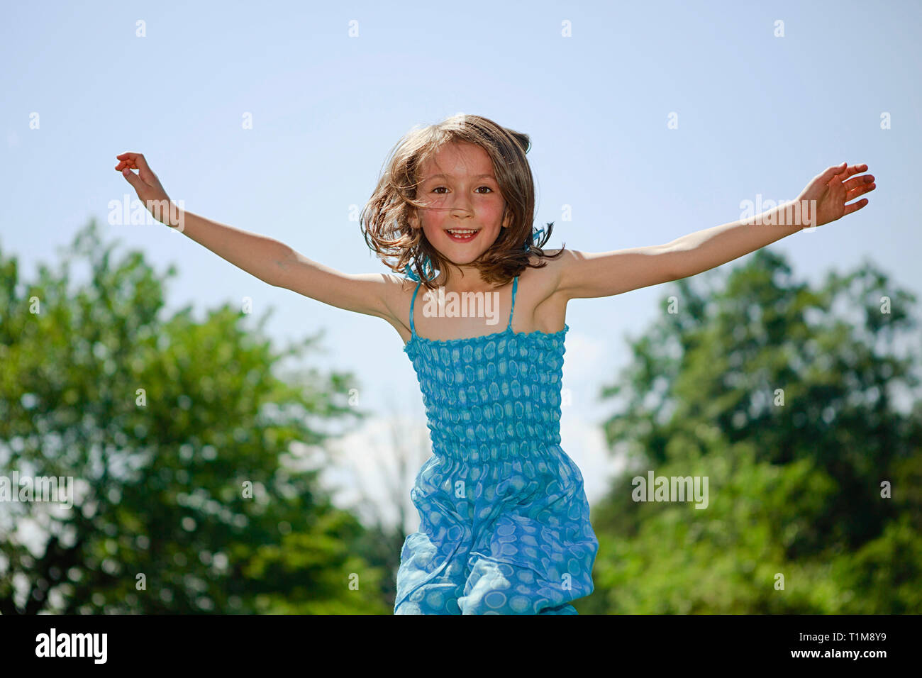 Portrait verspielten Mädchen mit ausgestreckten Armen vor Freude hüpfend im sonnigen Hof Stockfoto