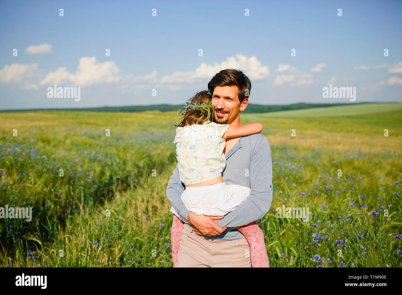 Portrait Vater hält Tochter auf sonnigem, idyllischem, ländlichem Feld mit Wildblumen Stockfoto