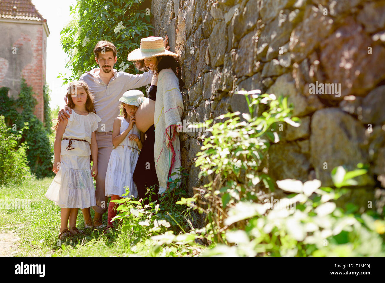 Portrait Schwangerer Familie an sonniger Steinmauer im Garten Stockfoto