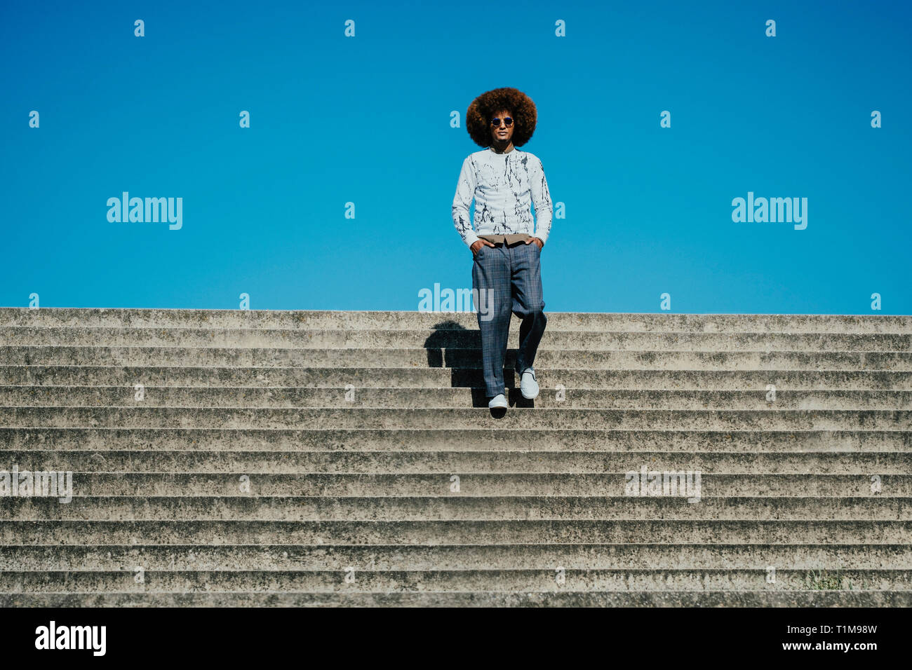 Portrait selbstbewusster, cooler junger Mann mit Afro auf sonnigen Stufen Stockfoto