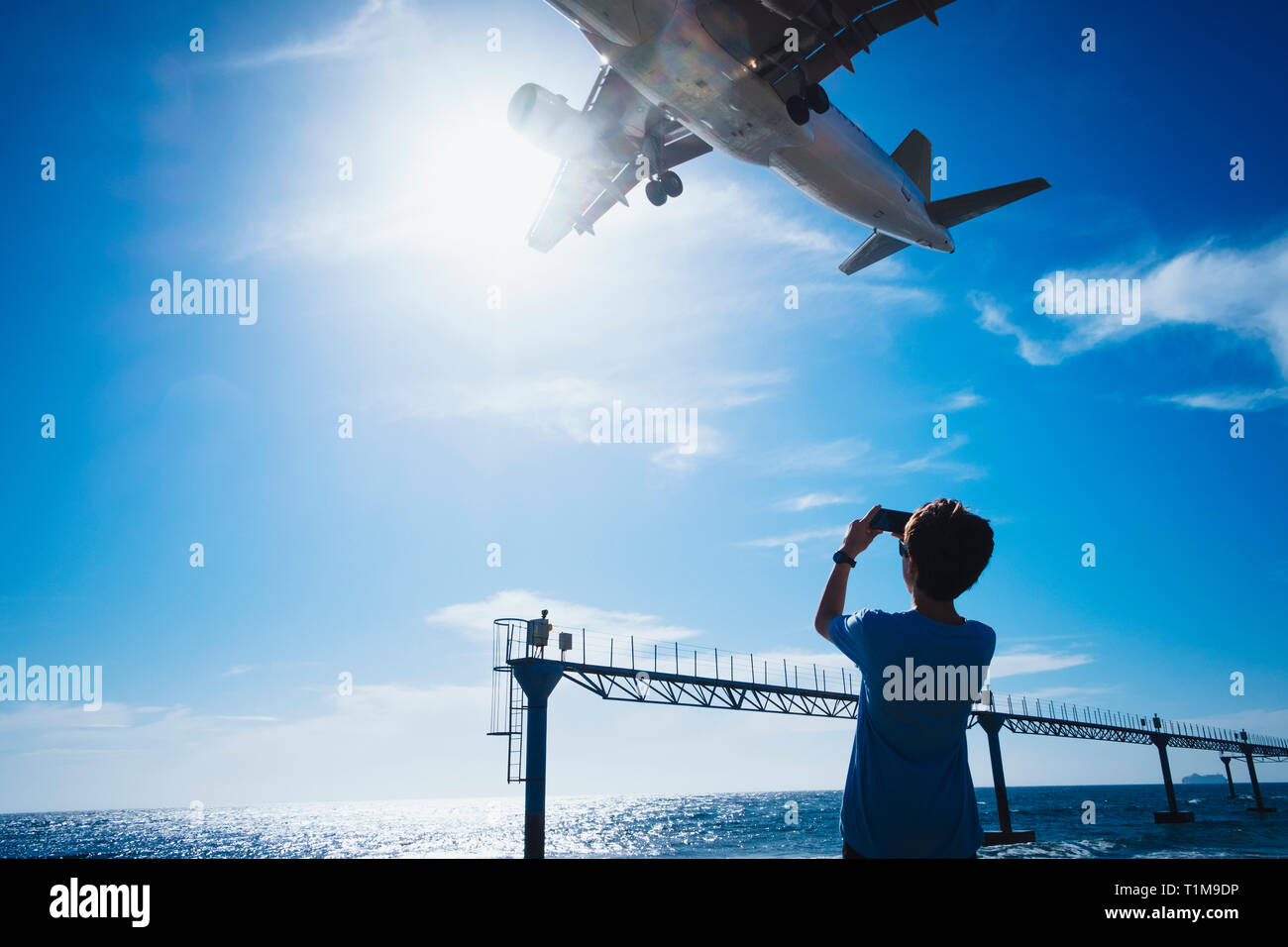 Junge mit Kameratelefon, der ein Flugzeug fotografiert, das tief oben in der Nähe des Flughafens von Lanzarote fliegt Stockfoto