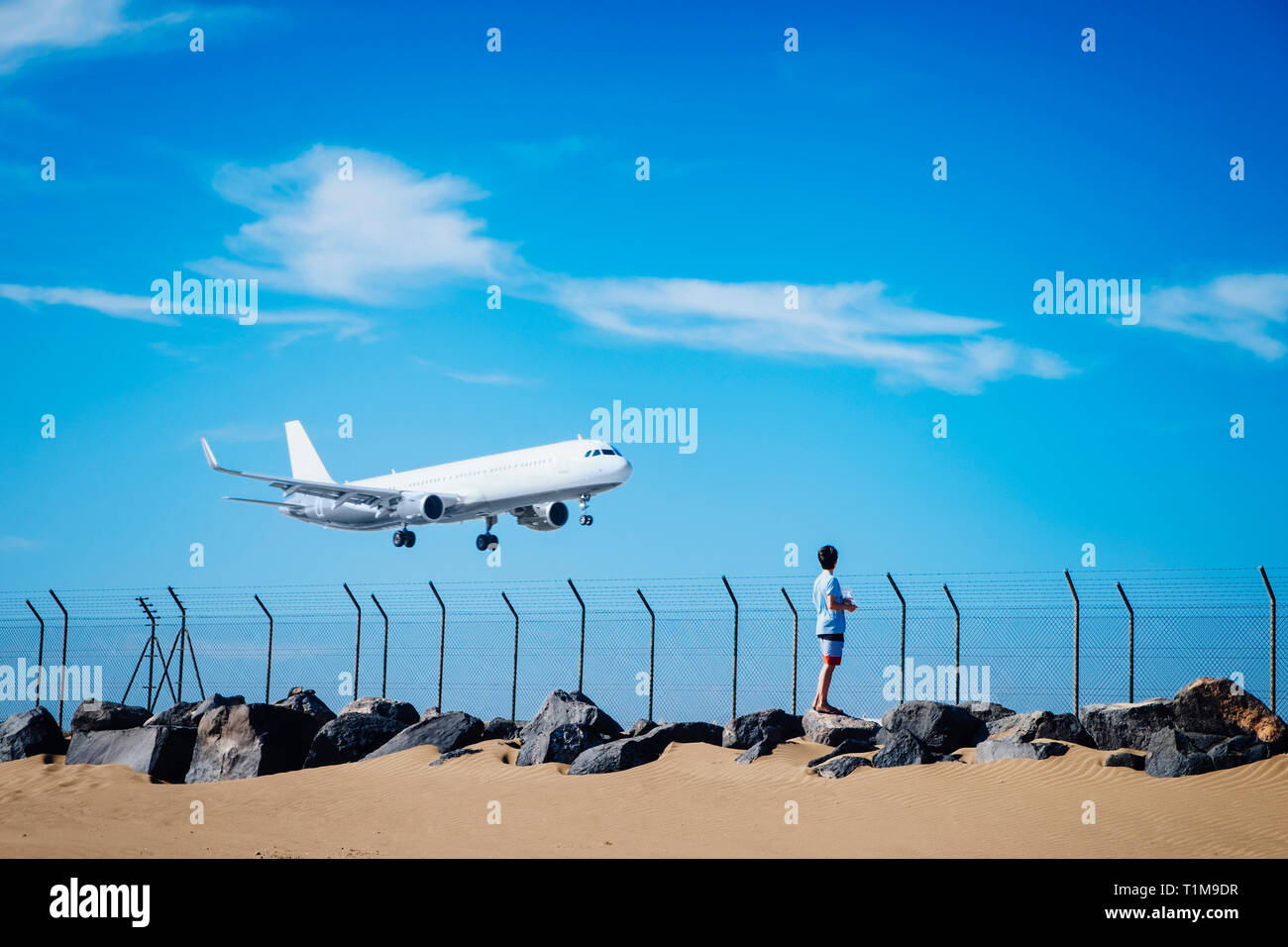 Junge am Strand, der das Flugzeug in der Nähe des Flughafens von Lanzarote, Spanien, beim Fliegen am blauen Himmel beobachtet Stockfoto