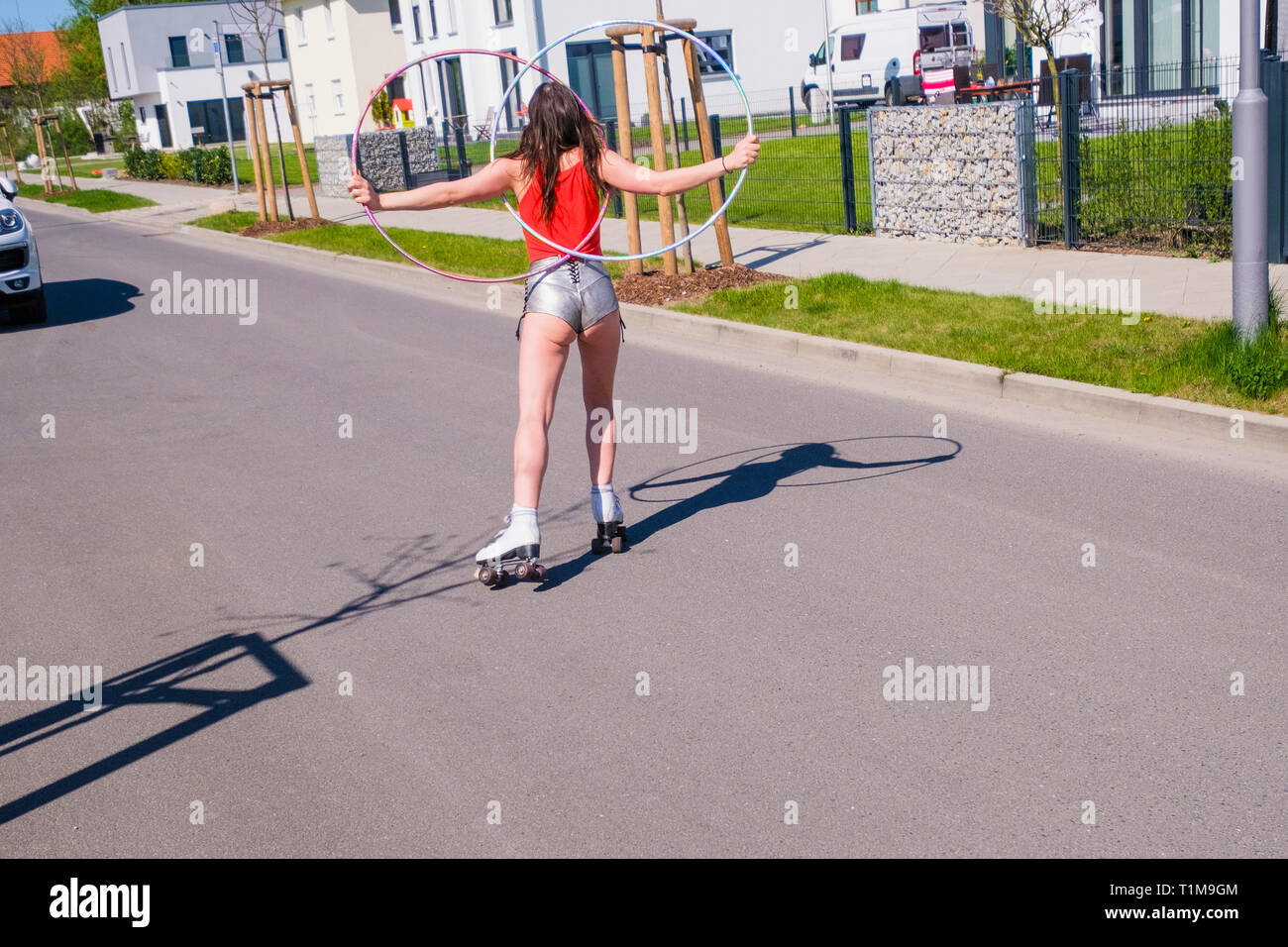 Frau in kurzen Shorts mit Kunststoffreifen Rollschuh-Skating auf der sonnigen Straße in der Nachbarschaft Stockfoto
