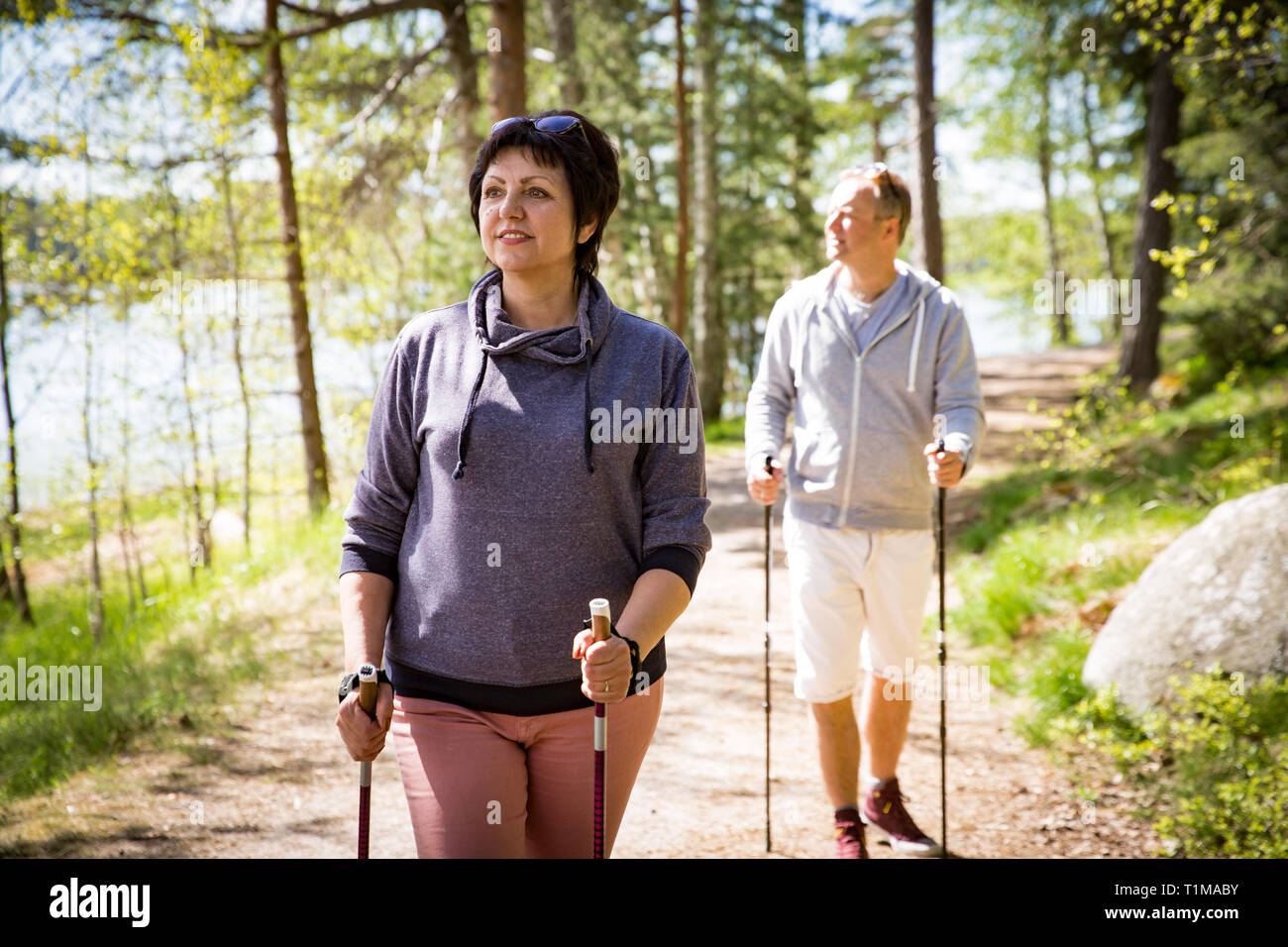 Sommer Sport in Finnland - Nordic Walking. Mann und reife Frau wandern im grünen sonnigen Wald. Aktive Menschen im Freien. Wunderschöne ruhige finnische Sommer la Stockfoto