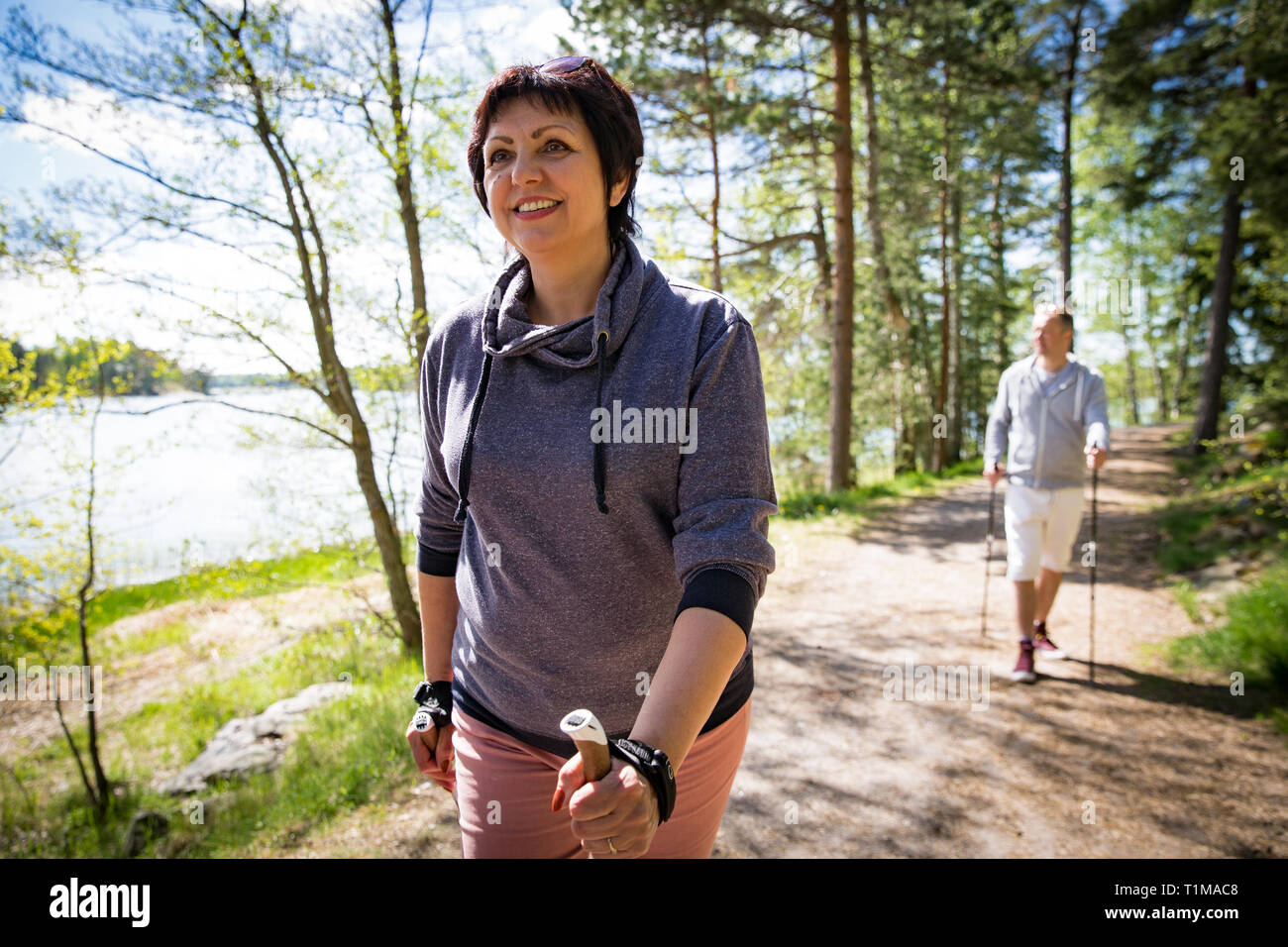 Sommer Sport in Finnland - Nordic Walking. Mann und reife Frau wandern im grünen sonnigen Wald. Aktive Menschen im Freien. Wunderschöne ruhige finnische Sommer la Stockfoto