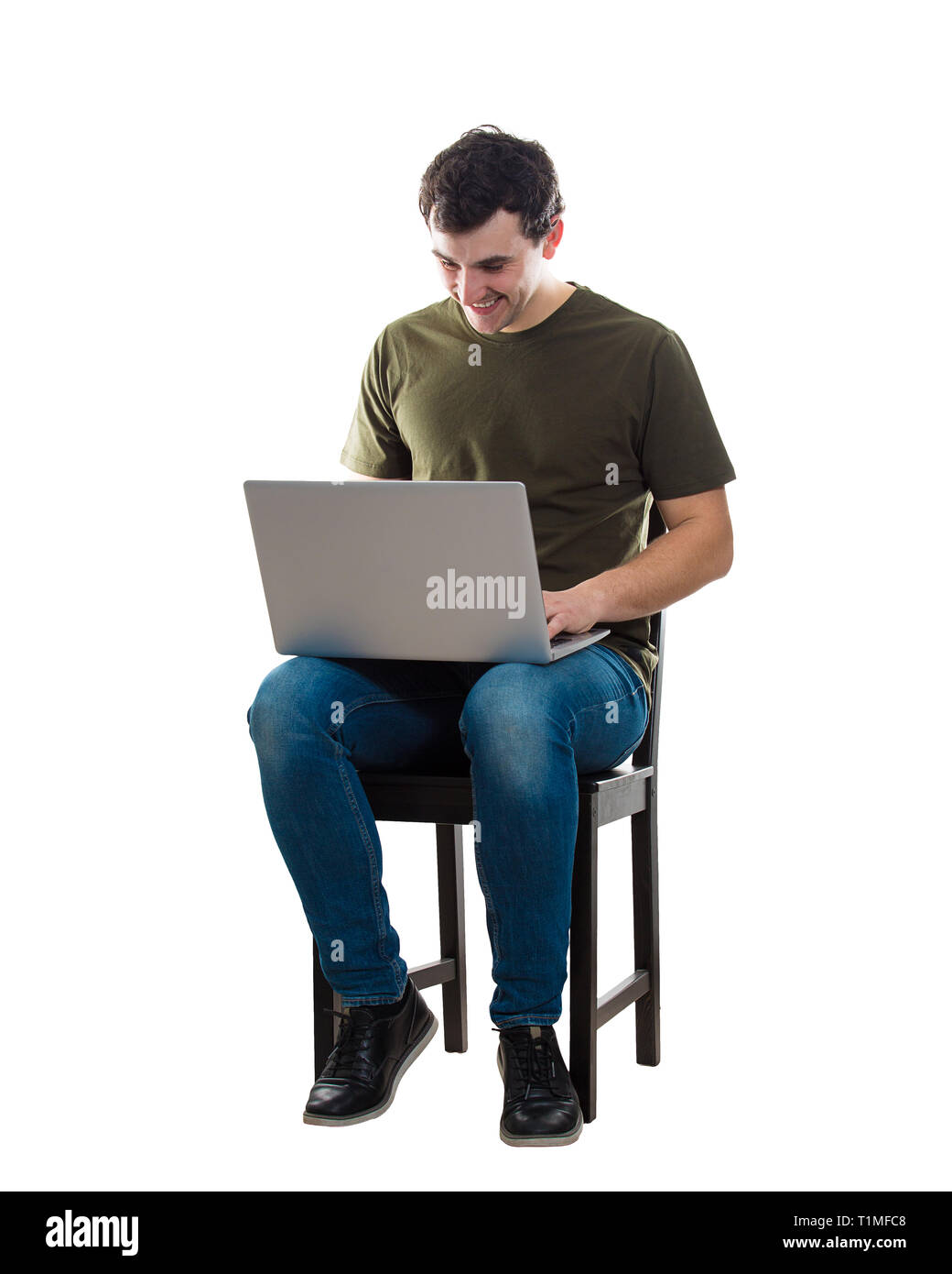 Fröhlicher junger Mann bei der Arbeit auf dem Laptop, auf einem Stuhl auf weißem Hintergrund sitzt. Kreative Freiberufler Kerl, die von zu Hause aus arbeiten an seinem Notebook compu Stockfoto