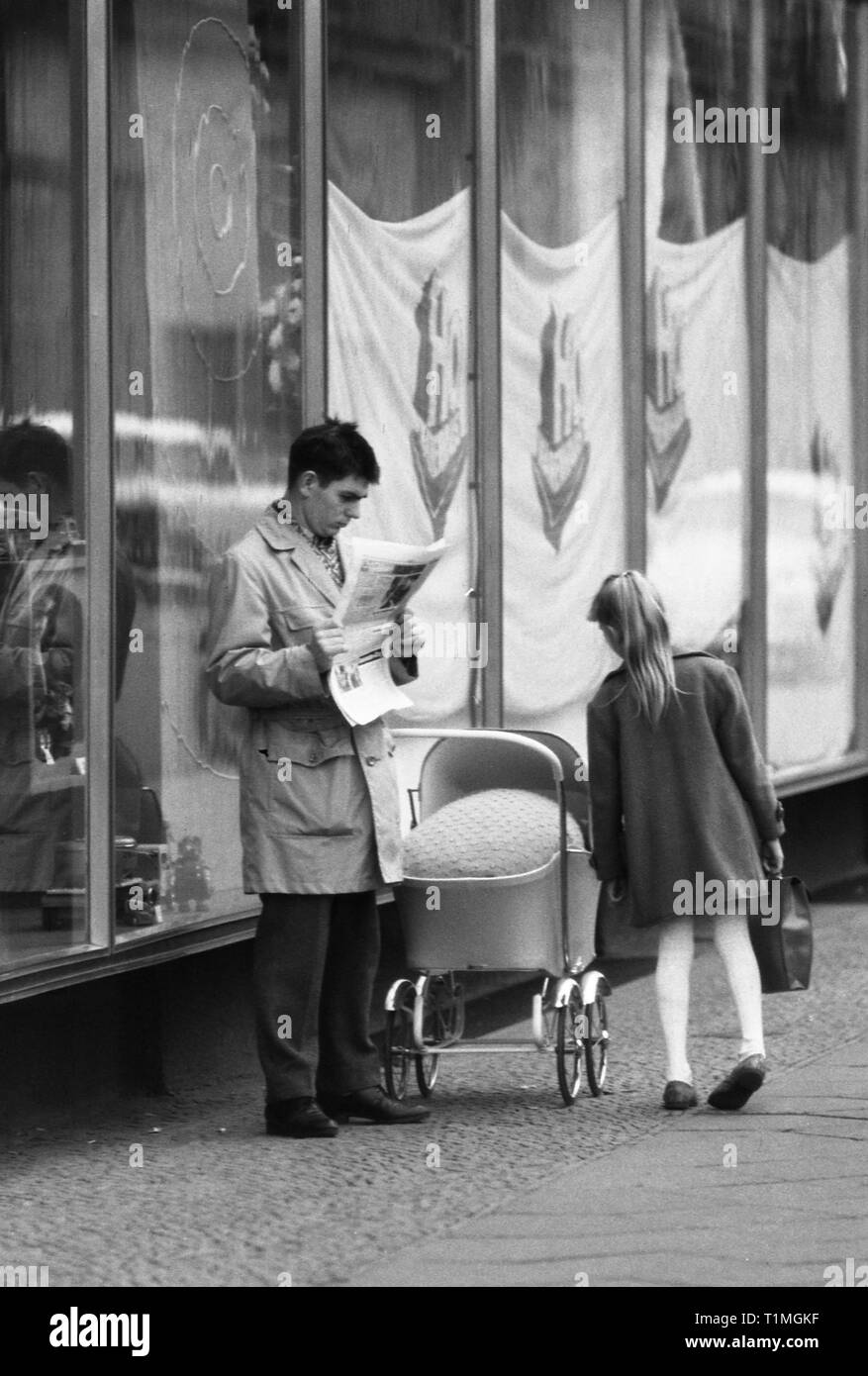 13.11.1965, Berlin, Berlin, DDR-Mädchen schaut in den Kinderwagen einer Zeitung-lesen Mann. 00 S 651113 281 CAROEX.JPG [MODEL RELEASE: NEIN PROPERTY RELEAS Stockfoto