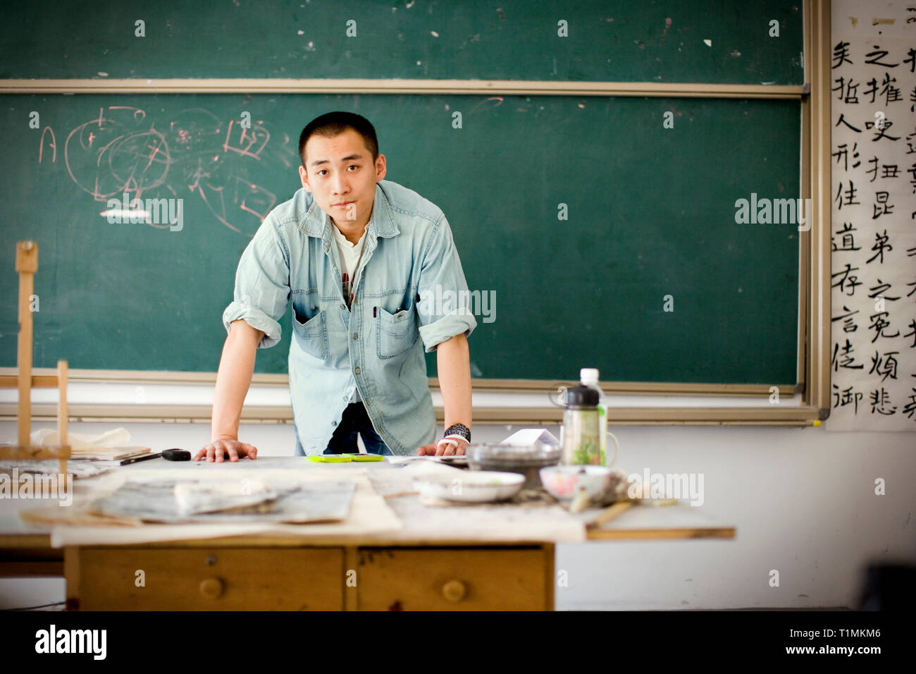 Porträt eines jungen erwachsenen Mann stand in der Nähe einer Kreidetafel in einem Klassenzimmer. Stockfoto