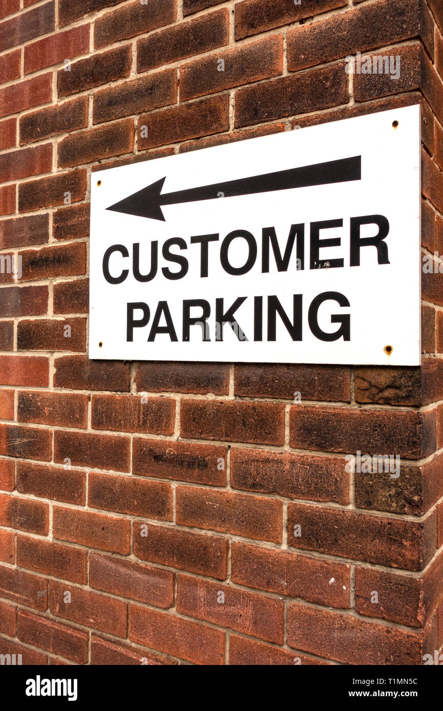 Weiß Kunden parken Schild mit schwarzer Schrift auf einem roten Ziegelmauer mit Pfeil, der auf den Kundenparkplatz Stockfoto