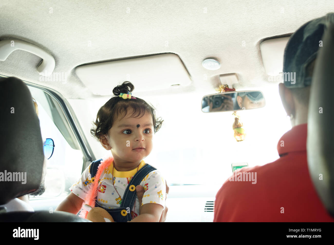 Einen schönen Indischen Baby Mädchen Kind im Auto vorne sitzen ist ein Blick auf die Fahrer mit einem netten Lächeln in einem fahrenden Auto. Indische Lebensstil Stockfoto