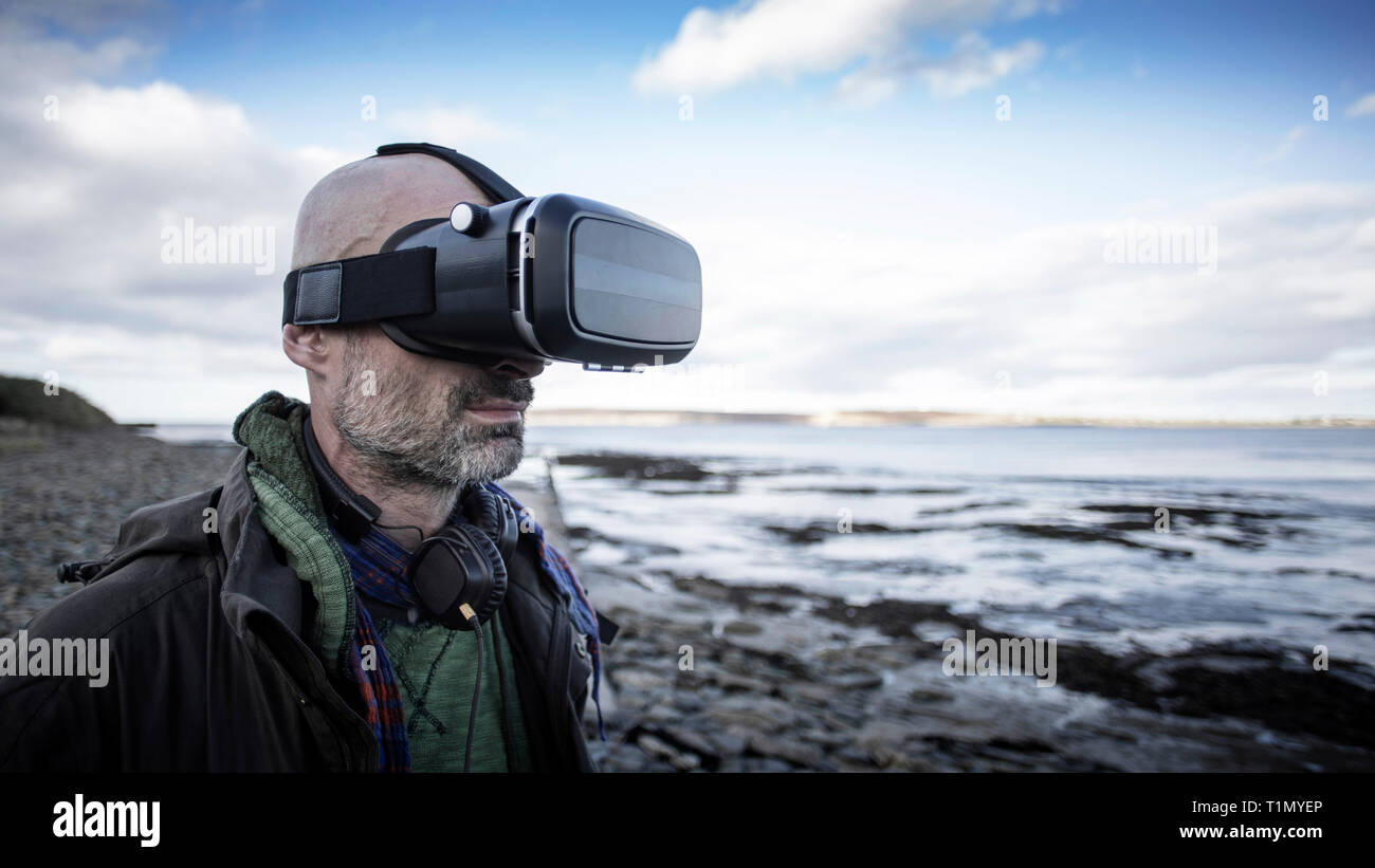 Eine Frontansicht Schuß eines reifen kaukasischen Mann mit einem Virtual reality Headset während an einem Strand im Vereinigten Königreich stehen, er ist Spaß zu haben. Stockfoto