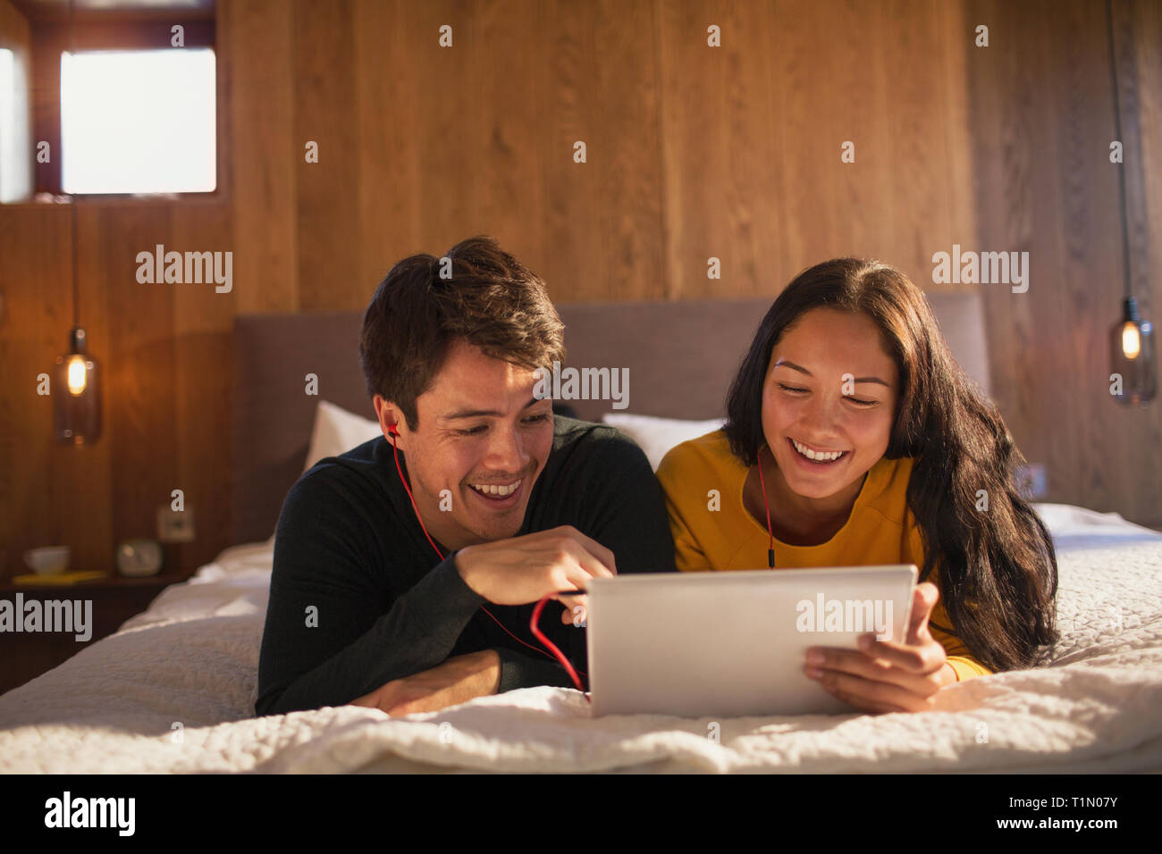 Glückliches junges Paar mit Kopfhörer gemeinsame Nutzung digitaler Tablet auf dem Bett Stockfoto
