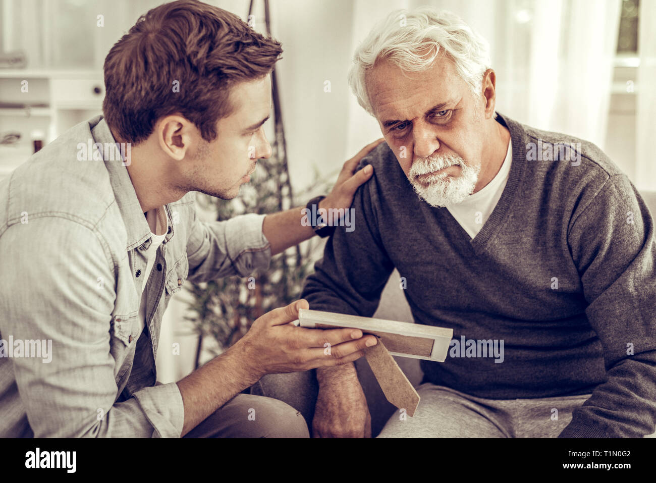 Erwachsener Sohn, der seine alten Vater einer Familie Foto zu. Stockfoto