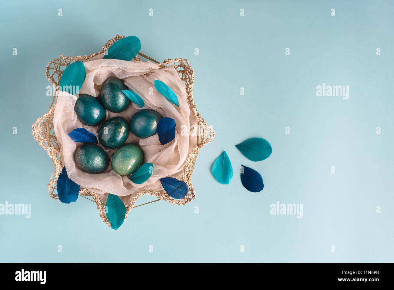 Ostern Hintergrund mit Eier in Blau, Türkis und Gold im Nest mit bunten blau und türkis Federn geschmückt. Ansicht von oben. Kopieren Sie Platz. Stockfoto