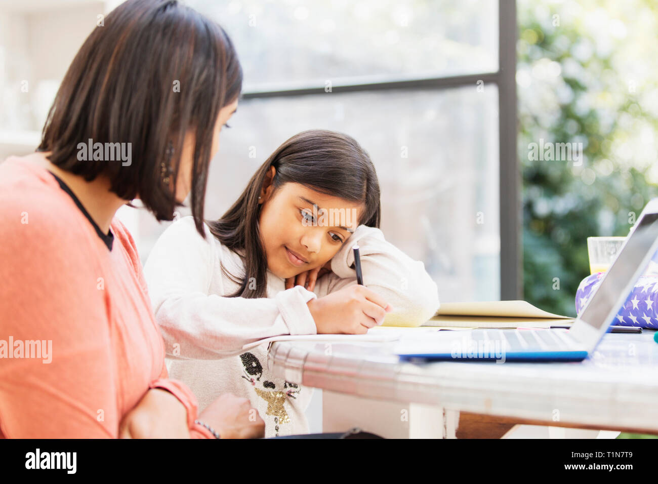 Mutter am Laptop ansehen Tochter Hausaufgaben am Tisch Stockfoto