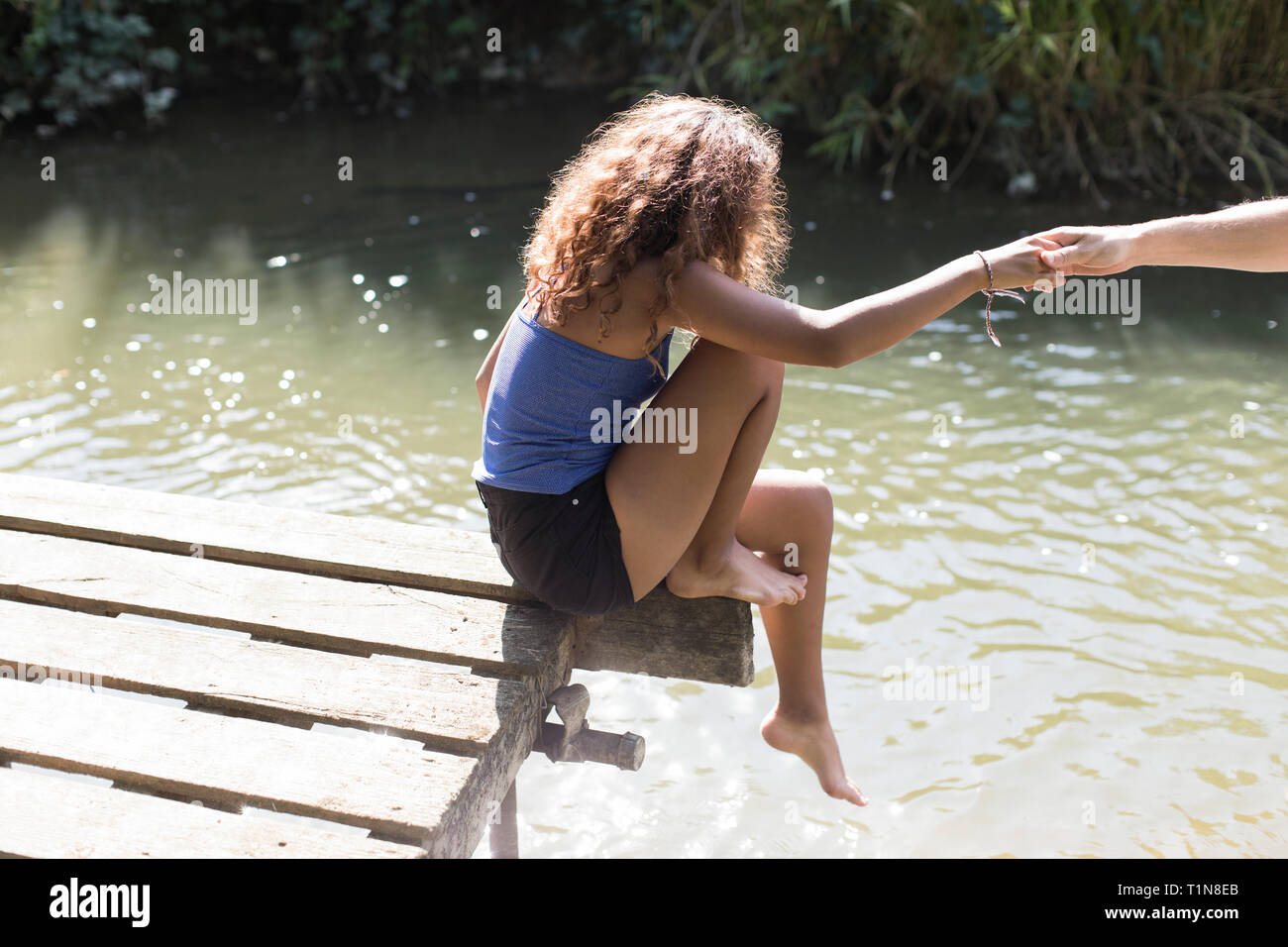 Mädchen sitzt am Rande der sonnigen Riverside dock Stockfoto