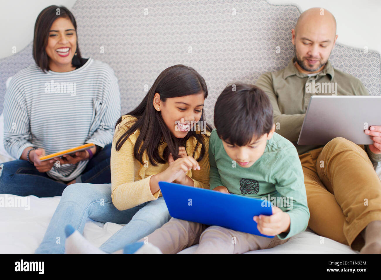 Glückliche Familie mit Technologie auf dem Bett Stockfoto
