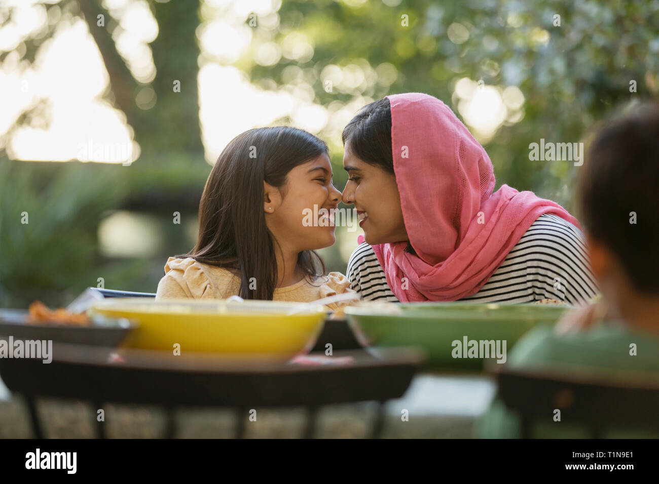 Liebevolle Mutter im hijab reiben Nasen am Tisch Stockfoto
