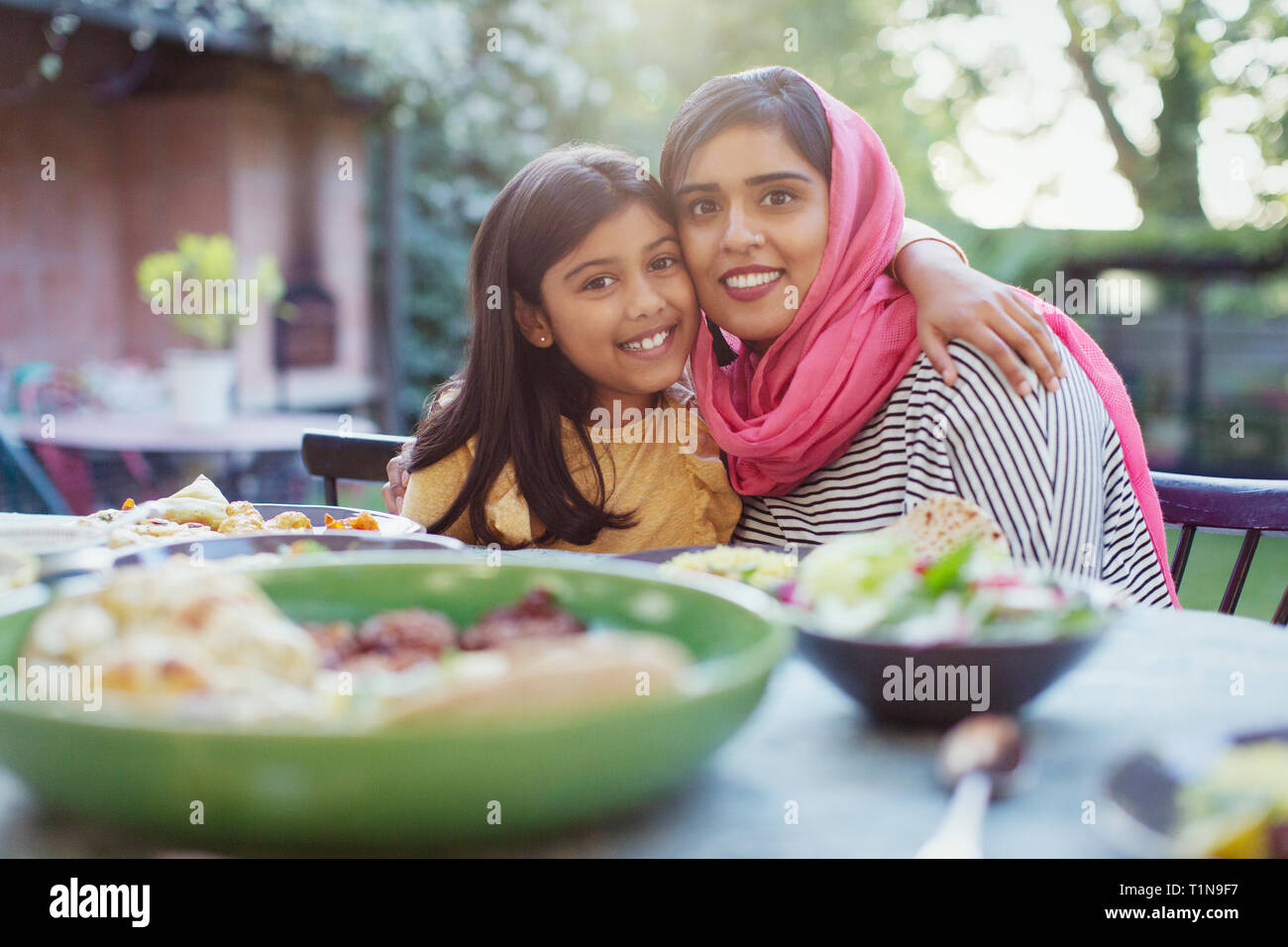 Portrait Happy Mother im hijab und Tochter umarmen am Tisch Stockfoto