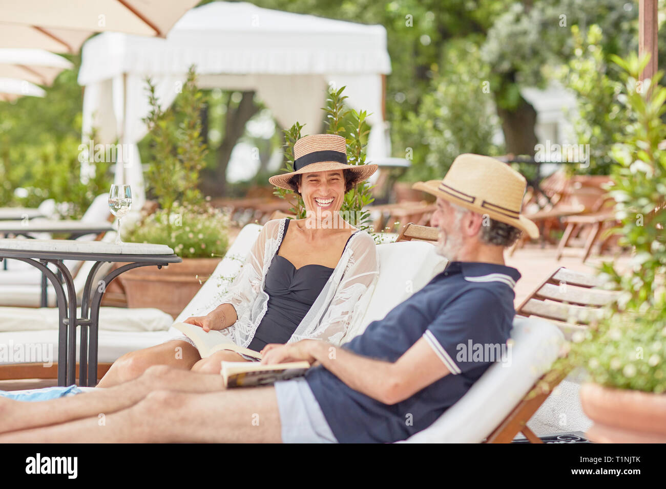 Reifes Paar Bücher lesen, entspannen Sie sich auf Liegestühlen im Resort Pool Stockfoto