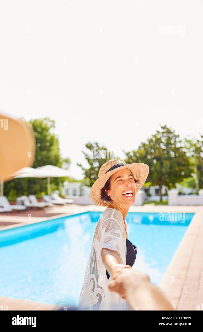Glückliche Ehefrau führenden Mann an der Hand bei Sunny Resort Pool Stockfoto