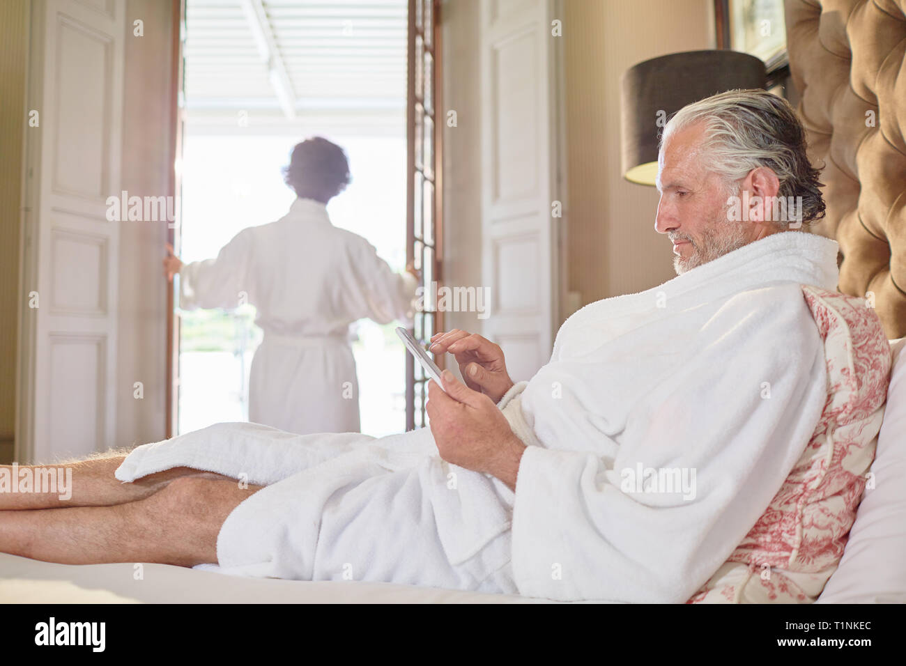 Reifer Mann im Spa Bademantel mit digitalen Tablette auf Hotel Bed Stockfoto