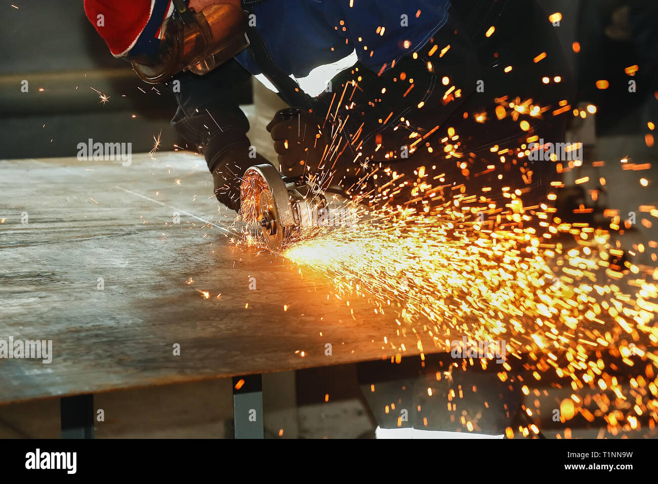 Ein Arbeiter in Handschuhe und Overalls schneidet ein Blech mit einem Winkel-Schleifmaschine. Die Funken von der Festplatte. Industriellen Hintergrund mit Platz für Kopie Stockfoto