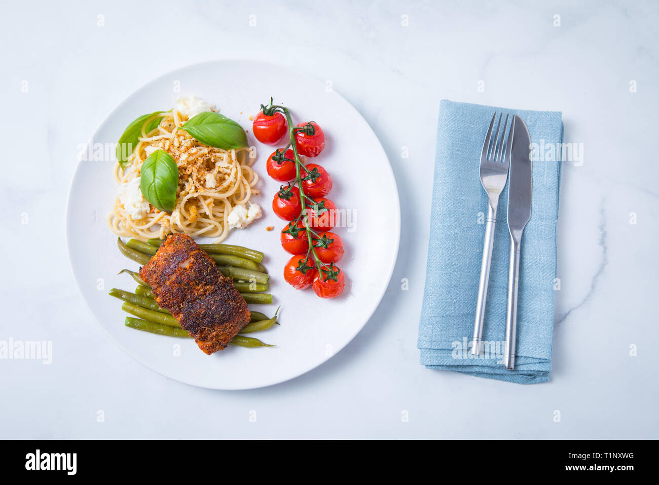 Geschwärzt cod auf grünen Bohnen, Weinstock und Kirschtomaten und plasta mit Käse und Basilikum auf einem weißen Teller mit Messer und Gabel mit einem weißen backgrou Stockfoto