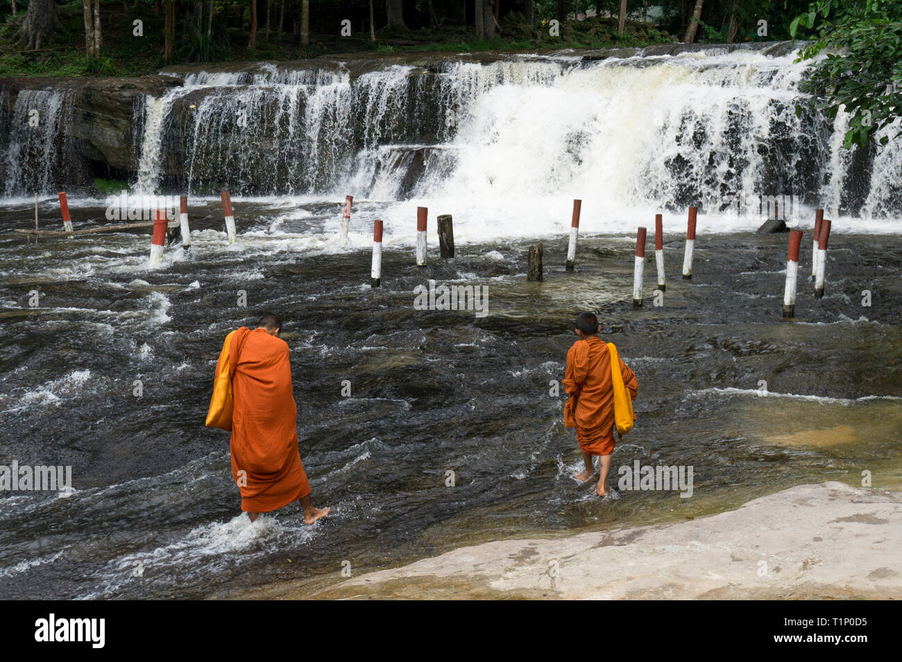 Zwei junge Mönche in orangefarbenen Gewändern ins Wasser mit einem Wasserfall im Hintergrund gekleidet Stockfoto
